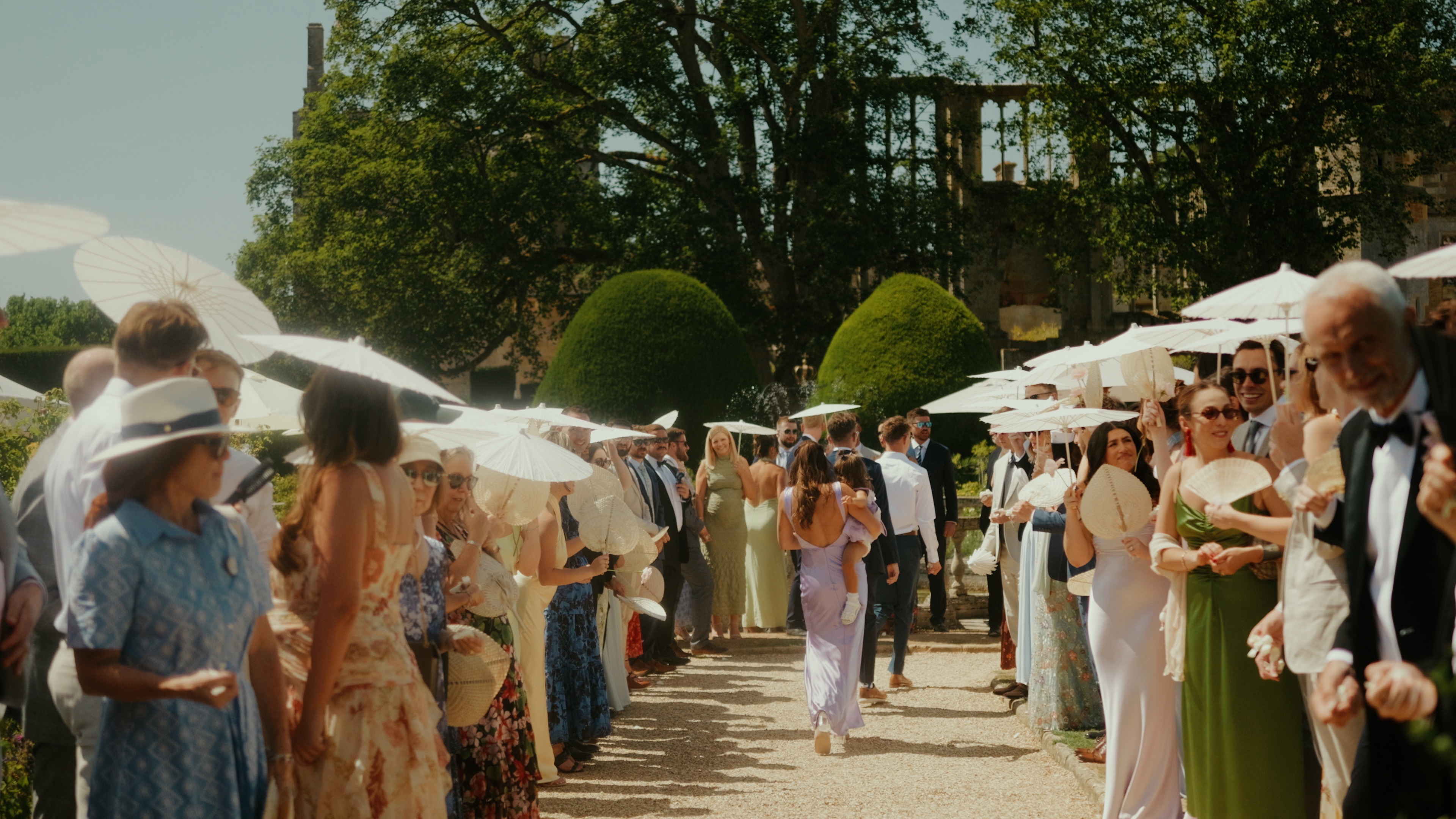 Wedding guests with parasols at outdoor summer wedding filmed by Alistair Kings